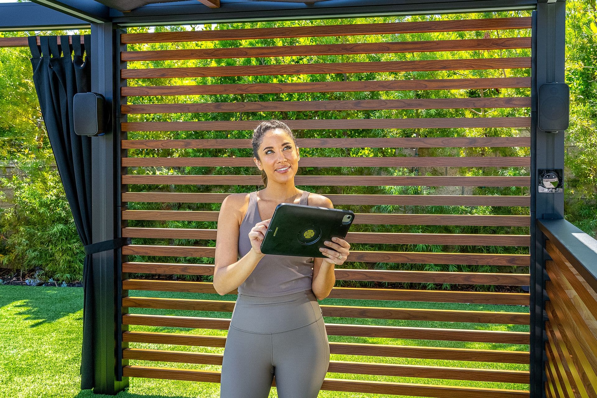 A woman in a pergola holding a tablet to control the pergola accessories.